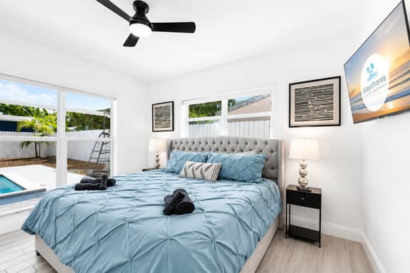 Bright king bedroom with pool views, TV, and serene coastal style